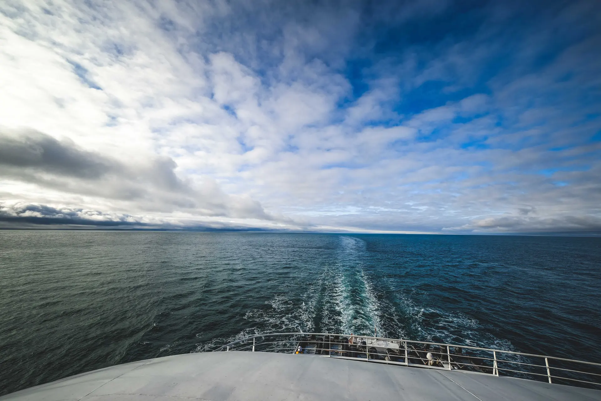 Majestic view from a ferry boat's bow showing the vast ocean under a partly cloudy sky.