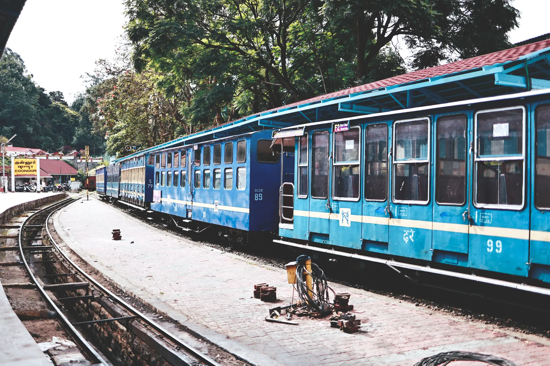 Scenic view of a blue train at Ooty Railway Station amidst lush greenery.
