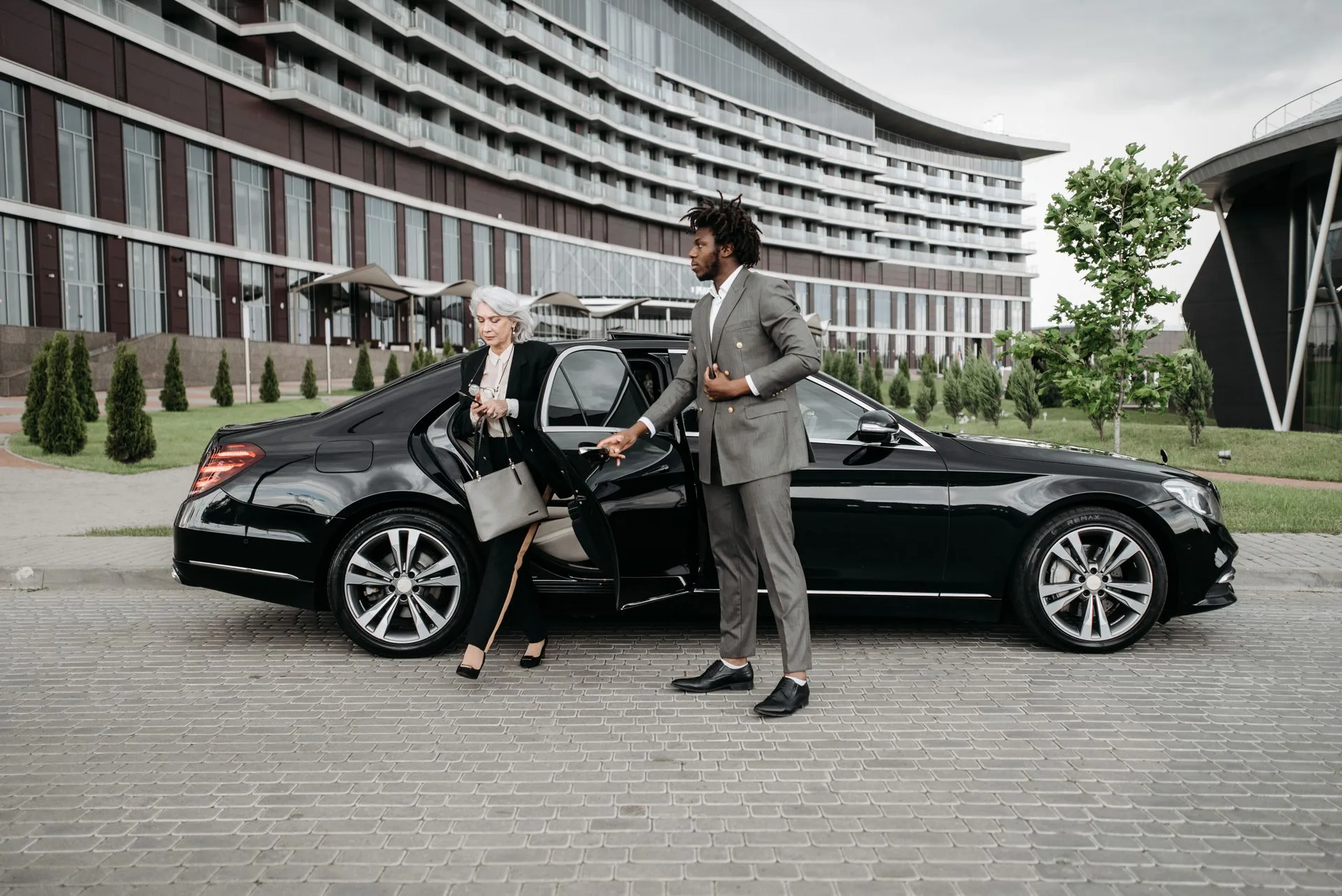 A chauffeur holds the door of a black sedan for a passenger.